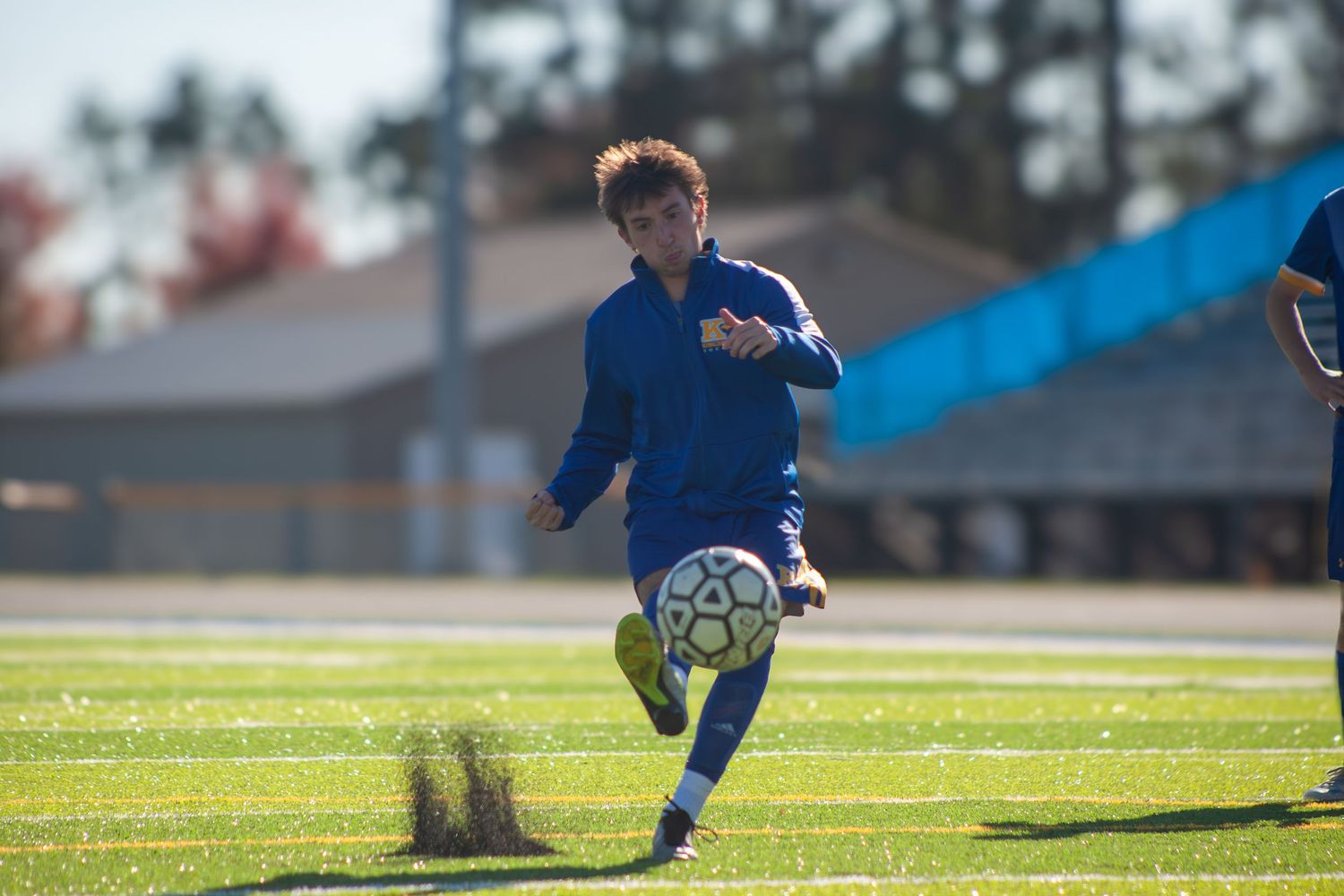 Soccer player in blue uniform practices ball control drills on sunny field.