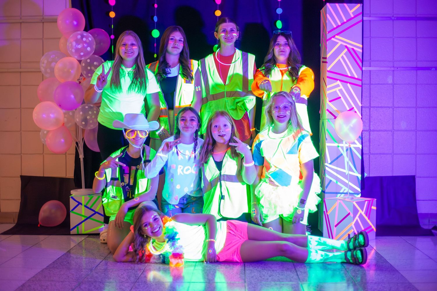 Group wearing neon outfits poses together under colorful lights at a glow party event.