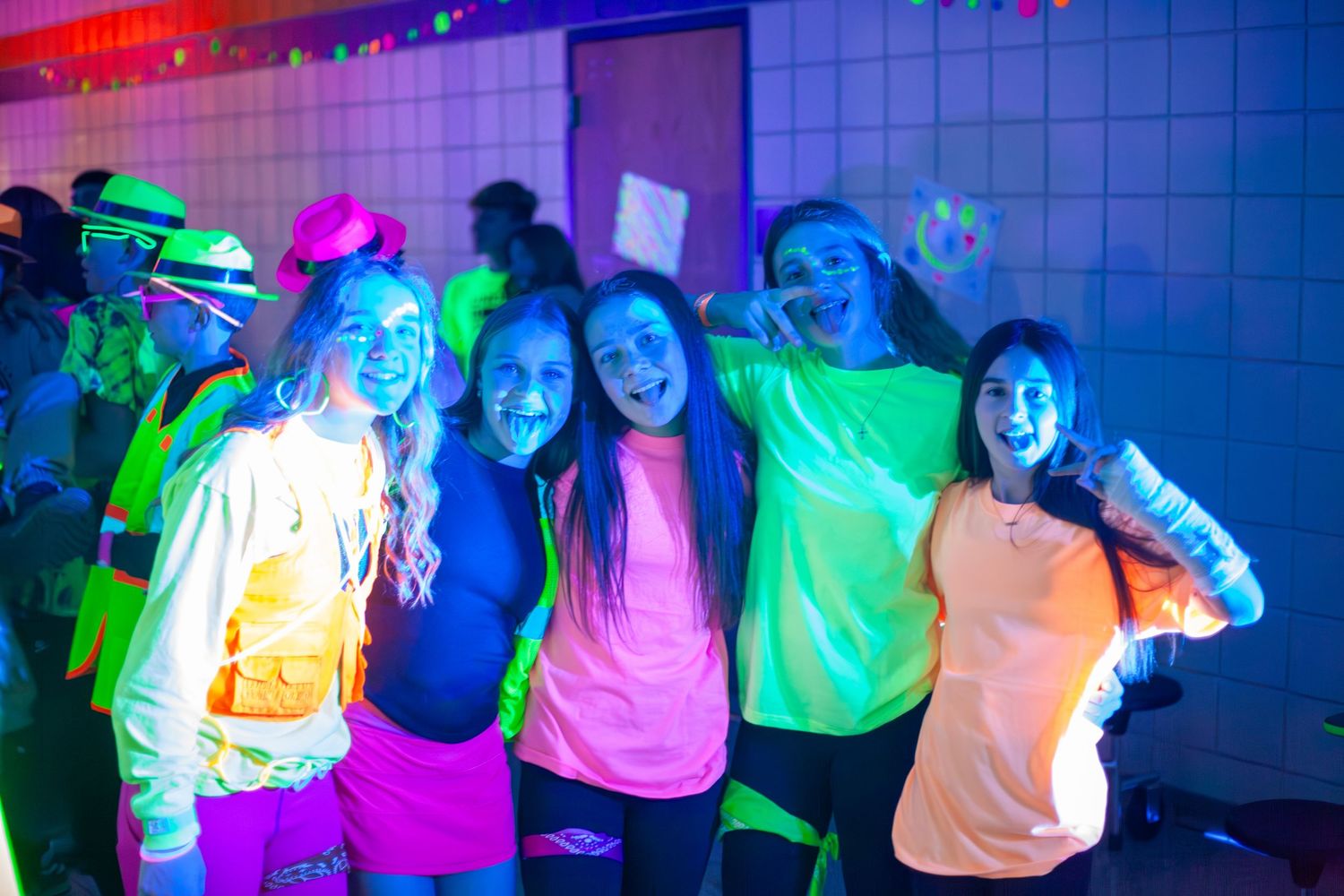 Group poses in neon clothing under colorful party lights.