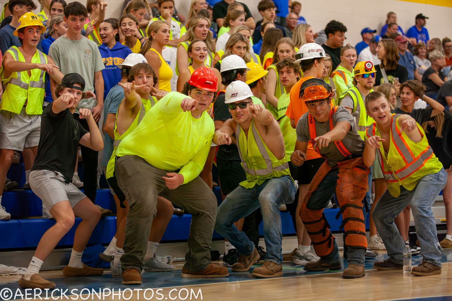 Enthusiastic crowd in yellow safety vests cheers during sporting event.