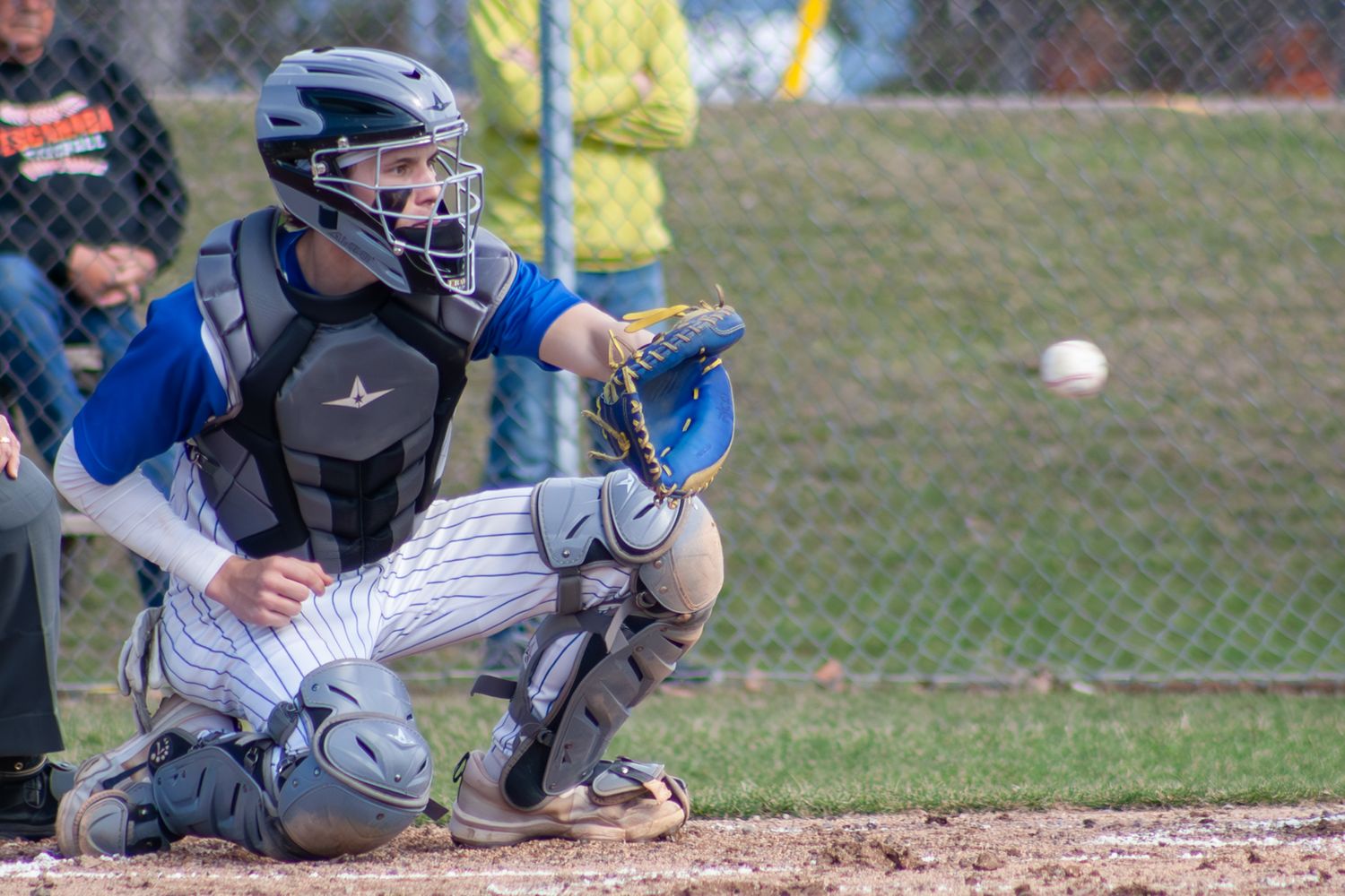 Baseball catcher in protective gear prepares to catch pitch during game.