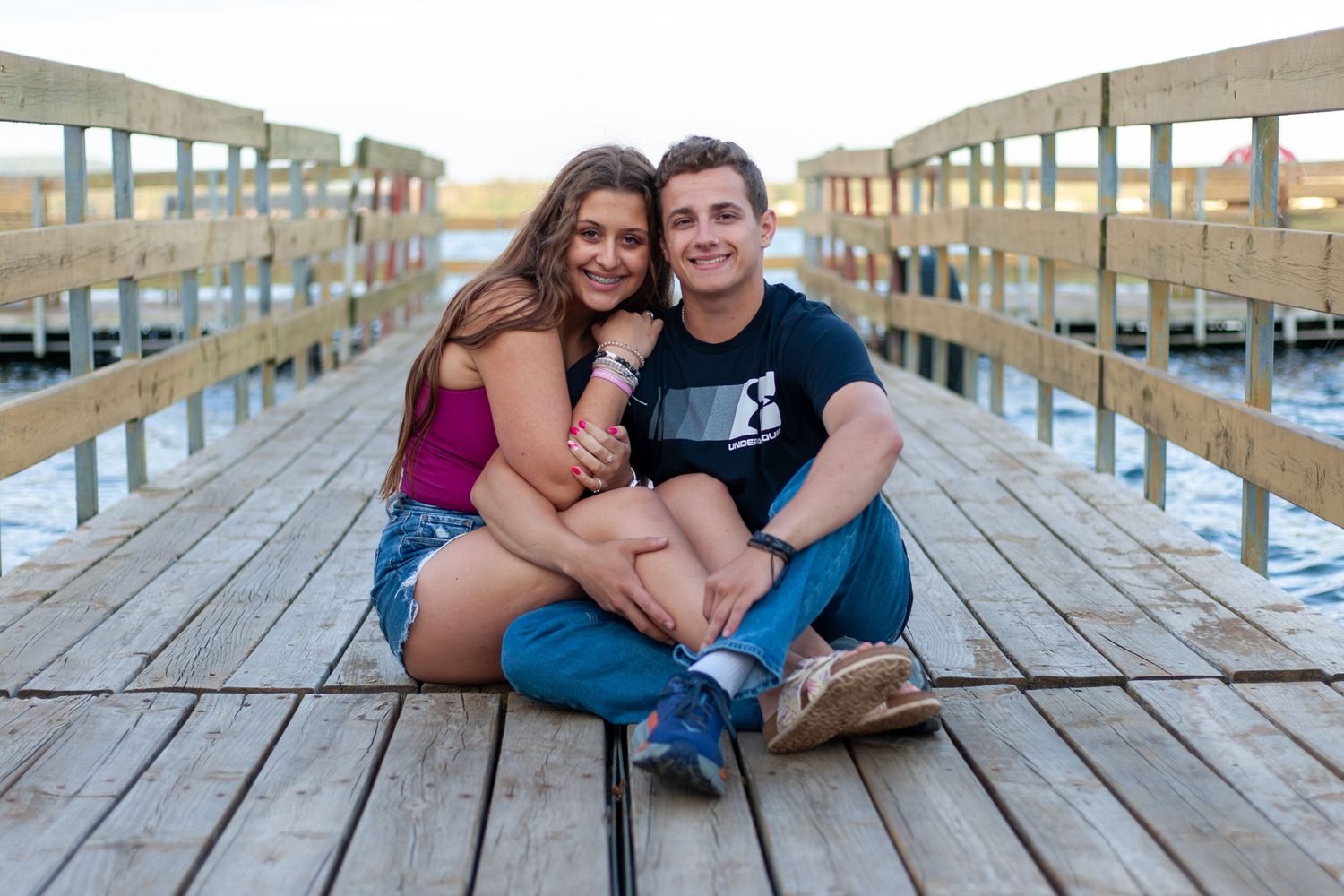 Couple sits together on wooden boardwalk during outdoor photo session.