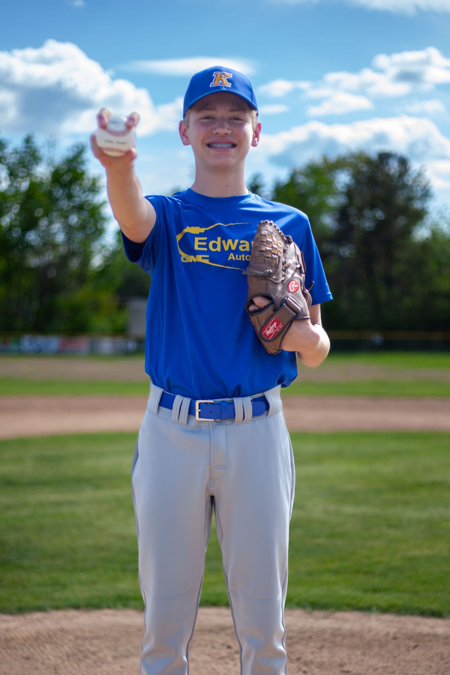 Baseball player in blue uniform holds up baseball while standing on pitcher's mound.