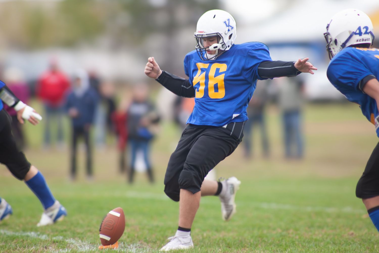 Youth football players in blue and black uniforms competing during a game on grass field.