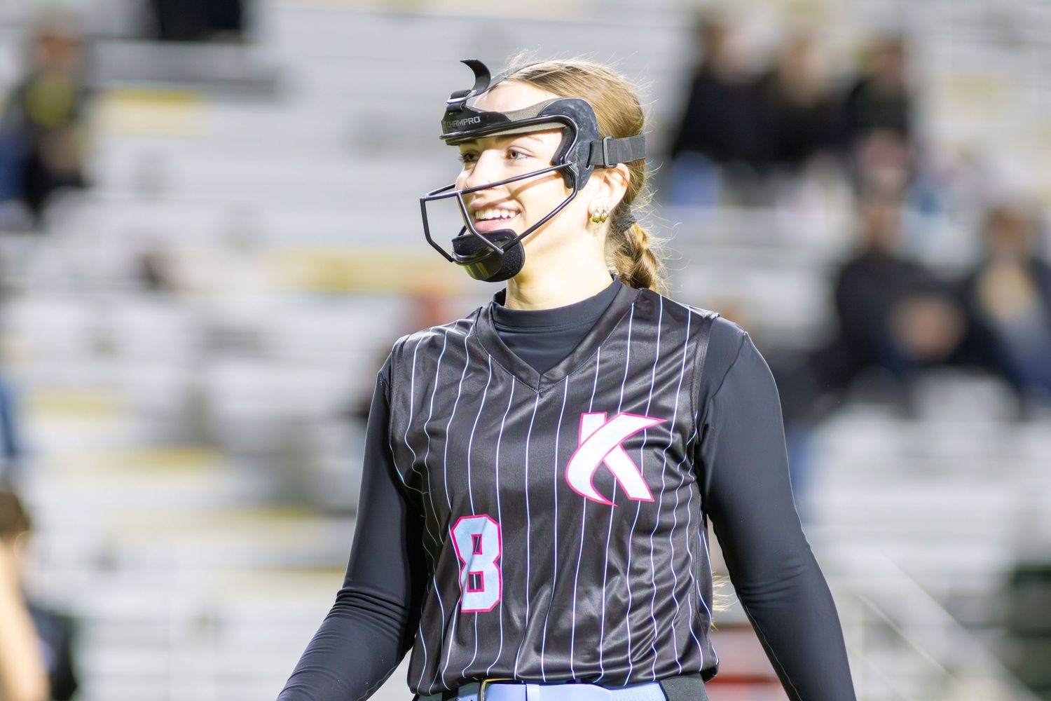 Female softball player wearing a black pinstripe jersey with number 8 and a protective face guard during a game.