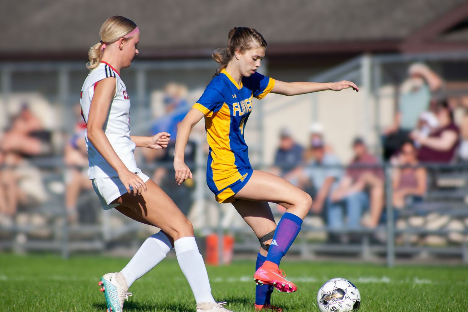 Two female soccer players compete for the ball during a sunny outdoor high school soccer game.
