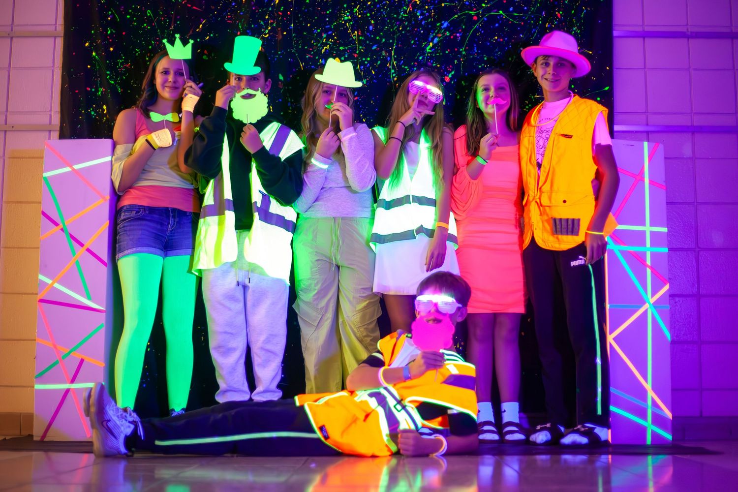 Students perform in colorful costumes on stage with neon lighting effects.