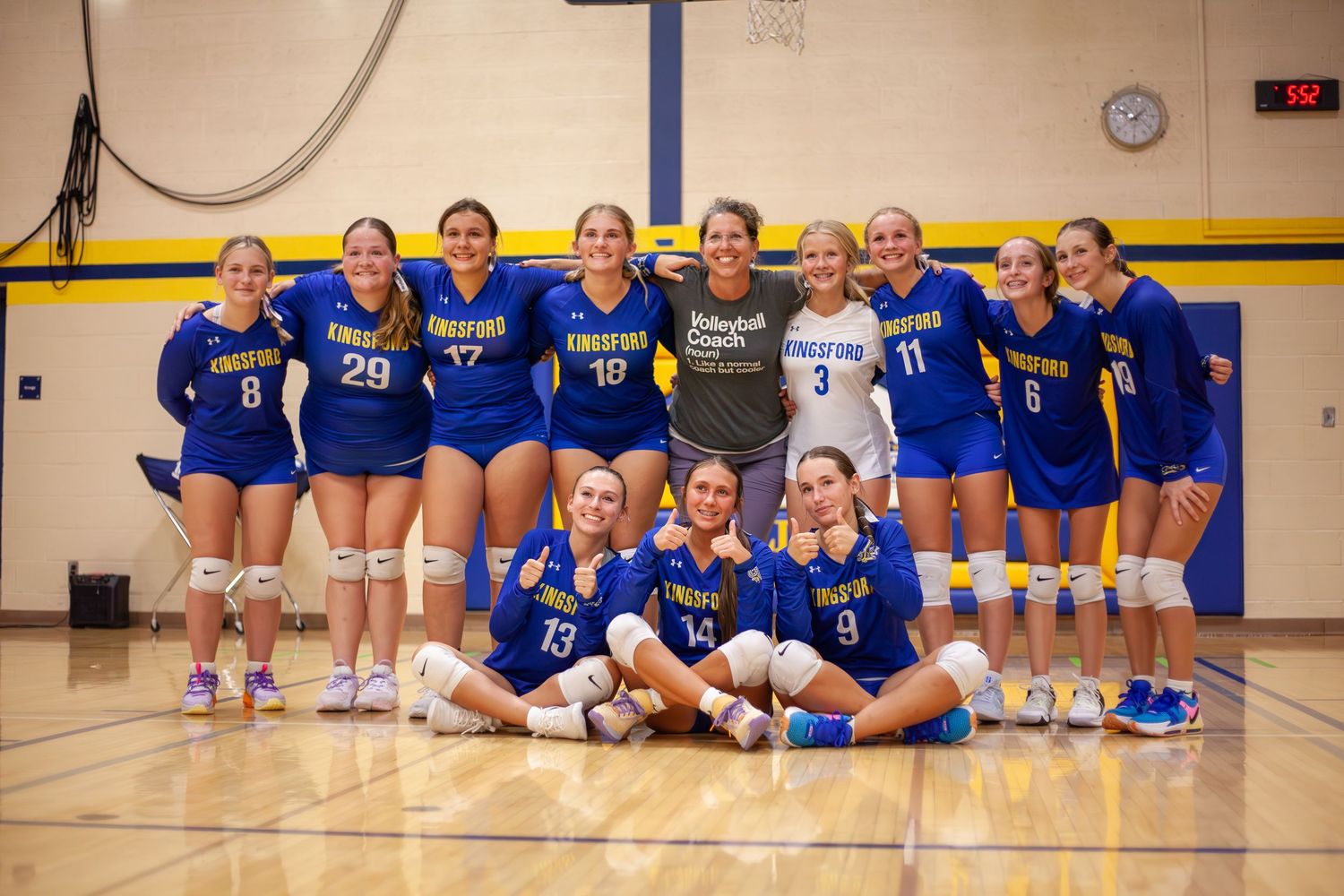 Women's volleyball team poses together in blue uniforms for group photo.