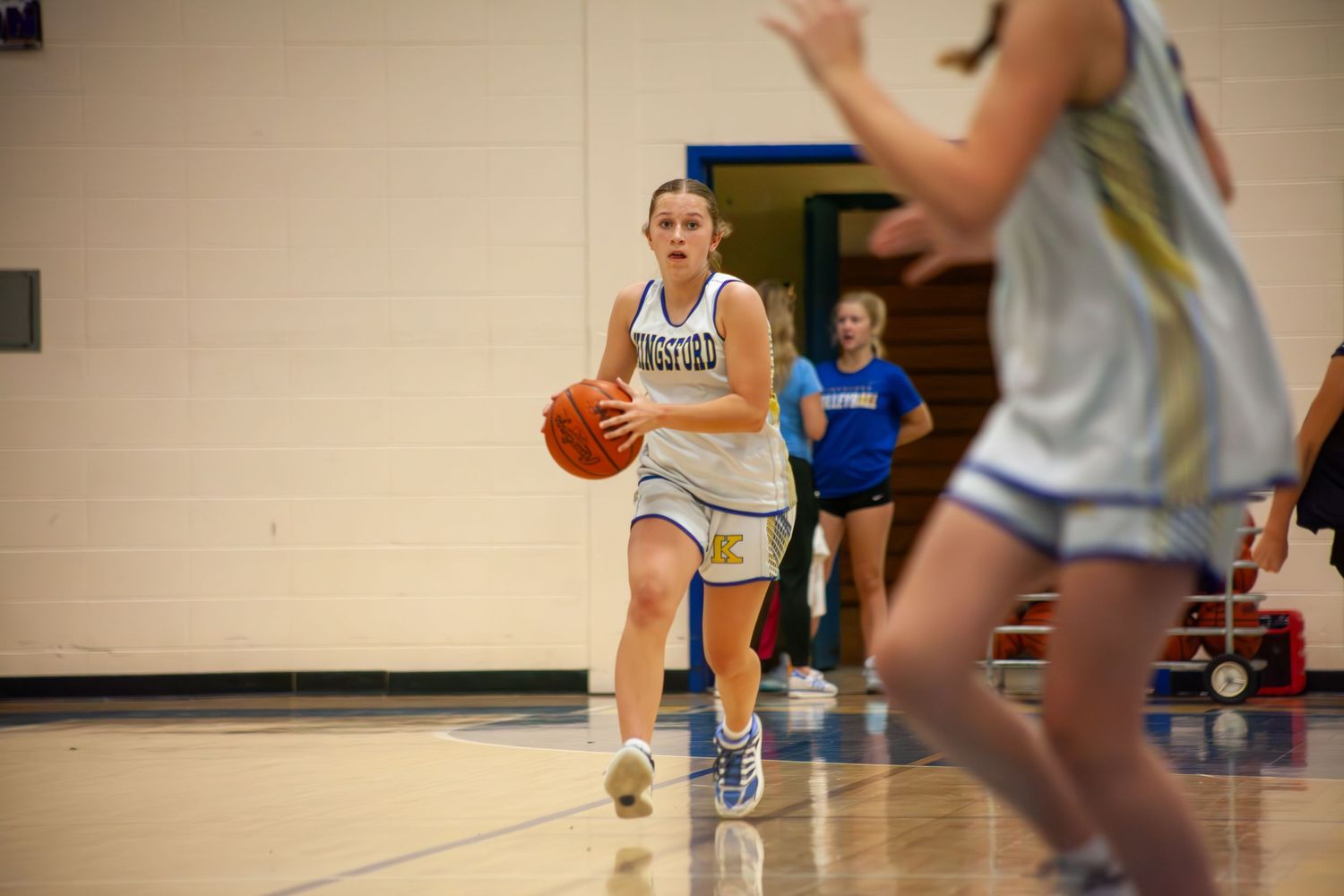 Basketball players practicing drills in a gymnasium with hardwood floors.