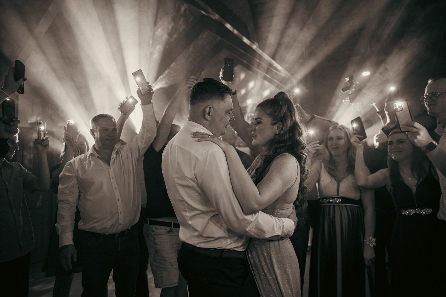 Newlyweds share romantic dance moment surrounded by guests and dramatic lighting at reception.