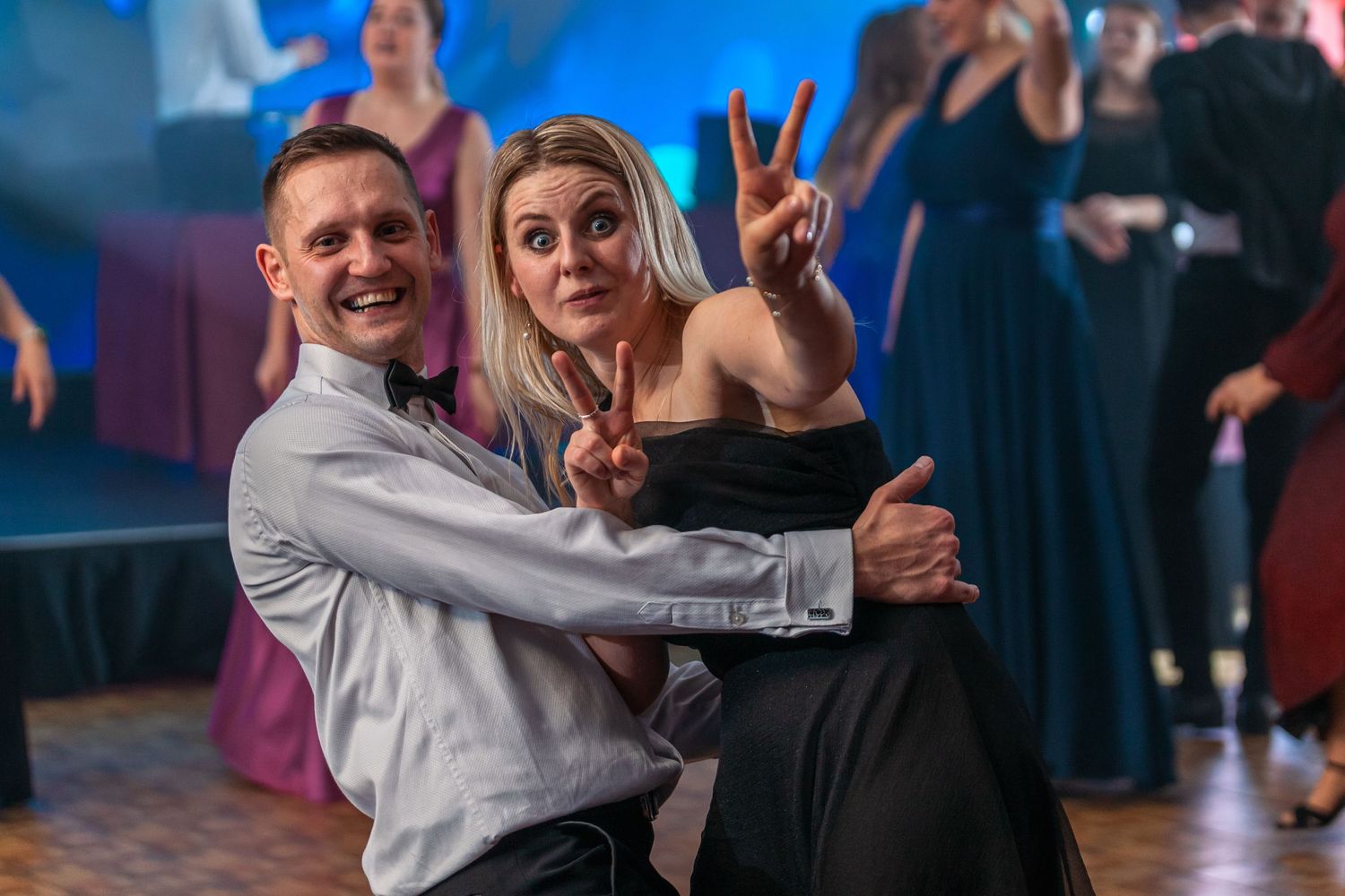 Couple dancing energetically at formal event with blue lighting.