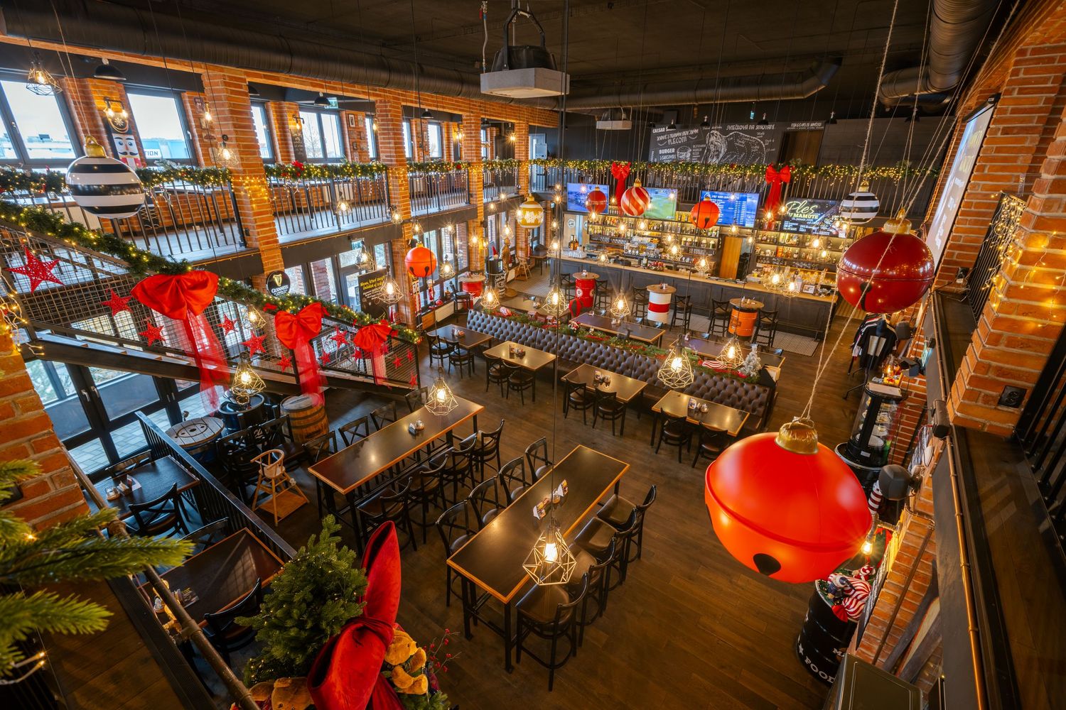 Modern restaurant interior with wooden decor, red pendant lamps, and industrial-style ceiling features.