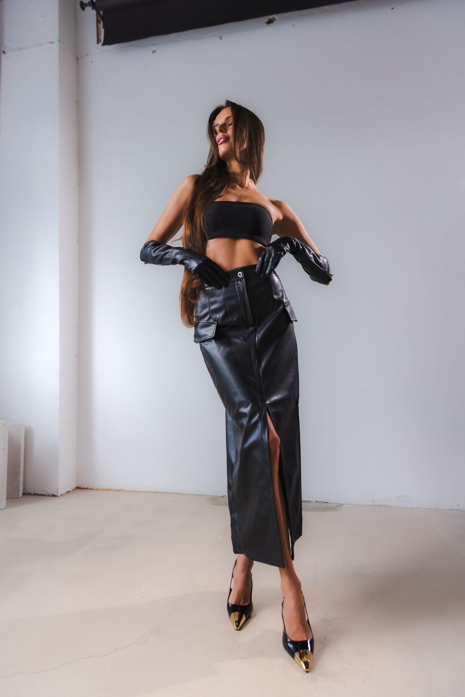 Model poses in a black leather dress and heels during a studio photoshoot.