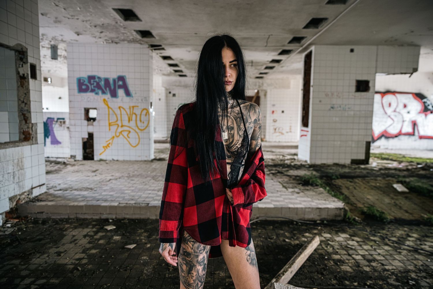 Urban exploration photoshoot in a dilapidated concrete building with red plaid shirt details.