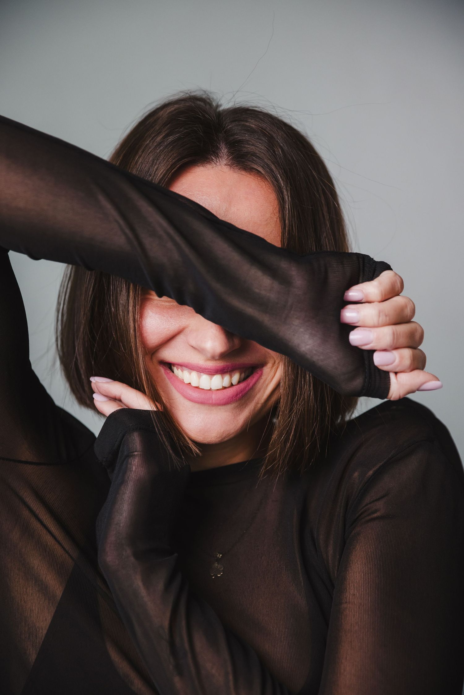 Playful portrait series showing person covering eyes with sleeves of dark sweater.