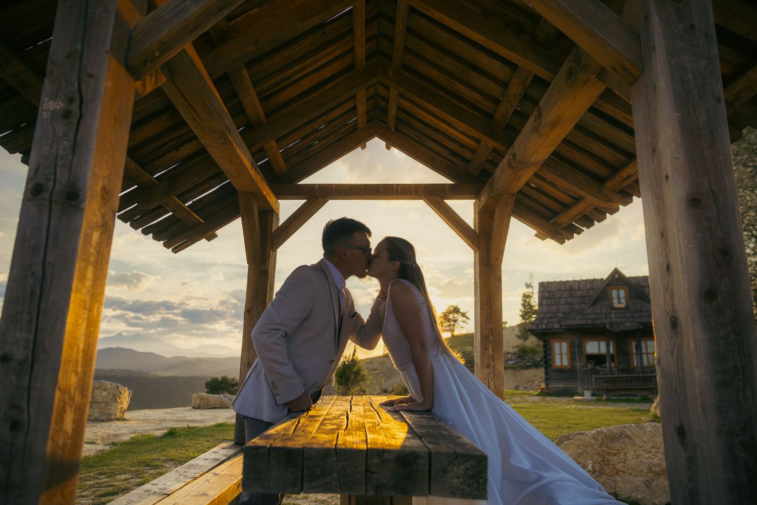 Wedding couple sharing intimate moment under rustic wooden shelter.