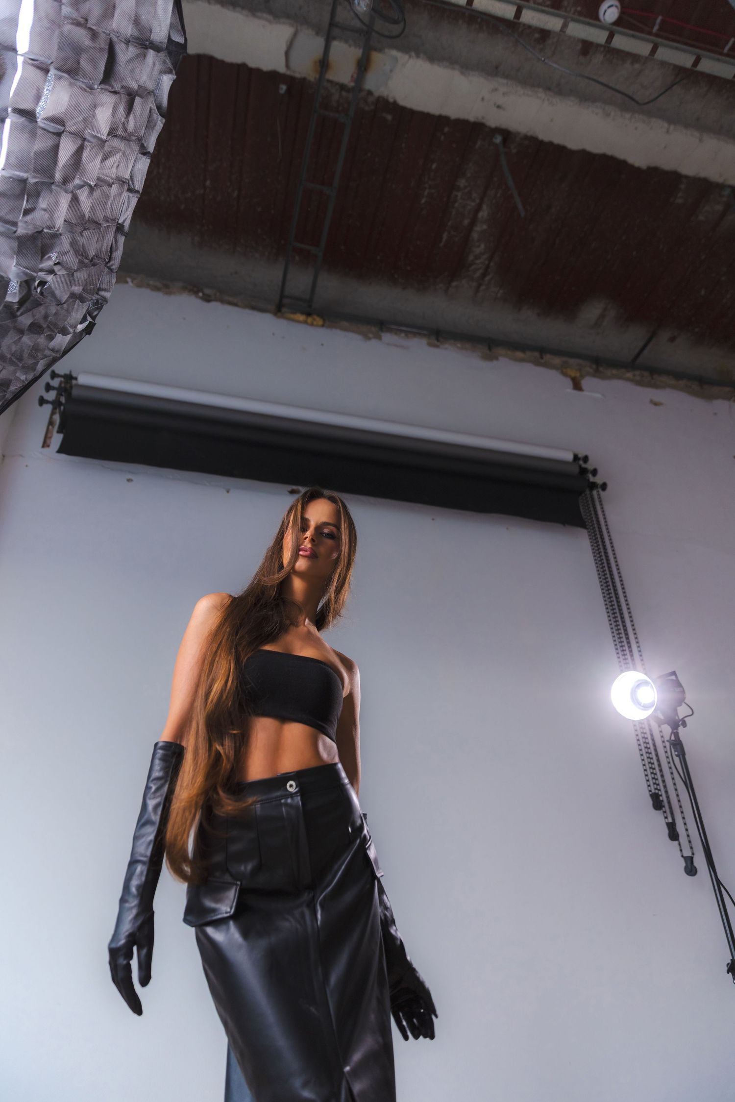 Fashion model wearing black leather outfit in minimalist white studio setting.