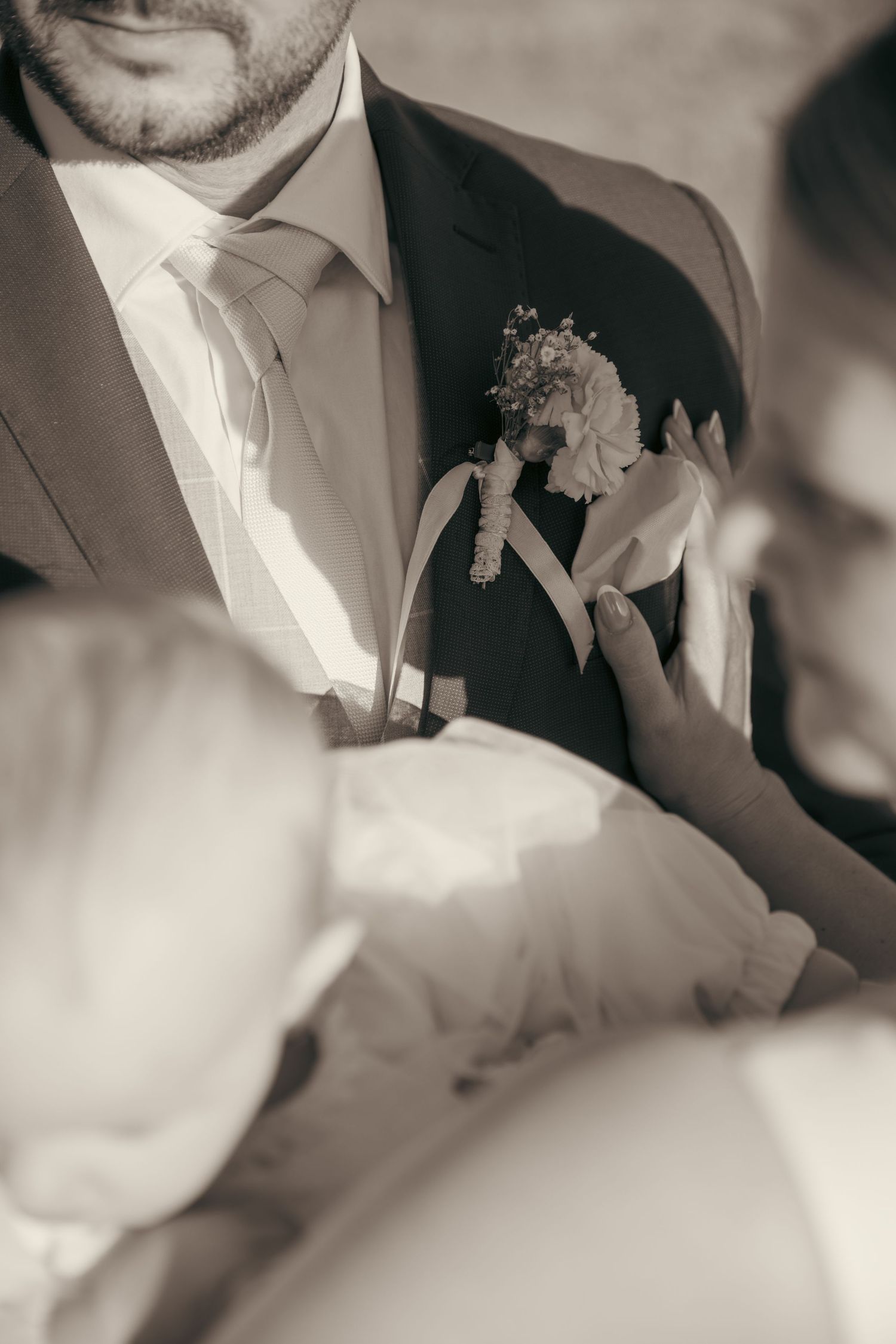 Close-up details of a groom's formal wedding attire in black and white.