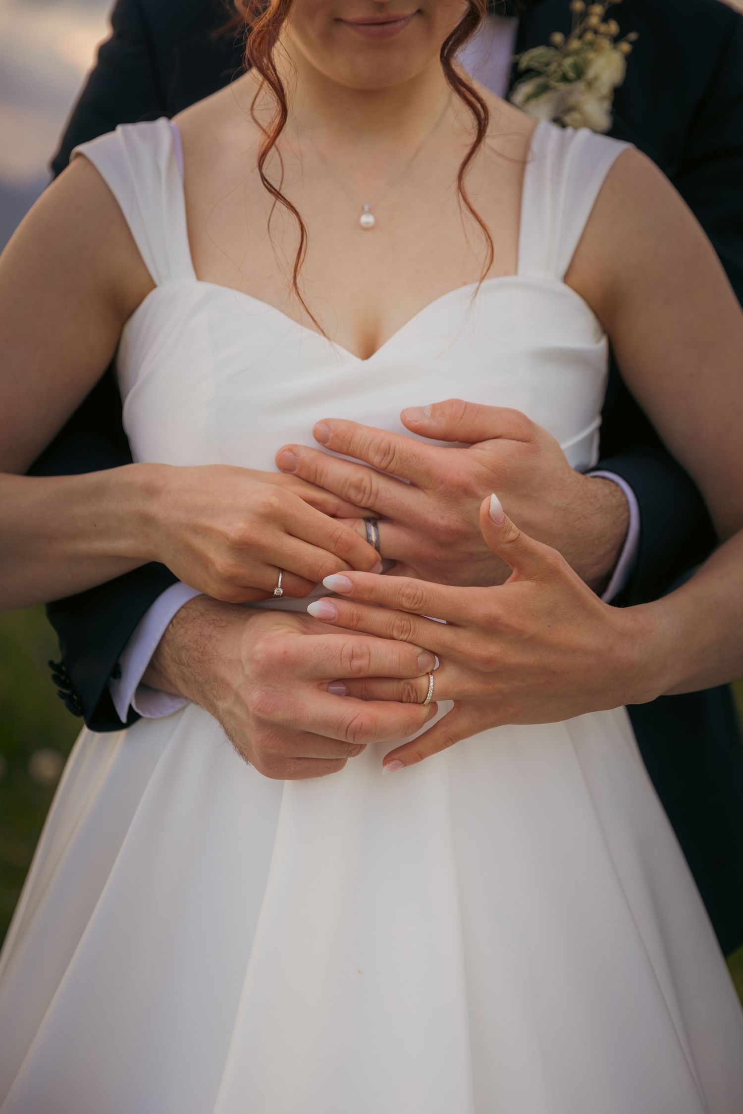 Close-up of bride's hands showing wedding ring and manicured nails.