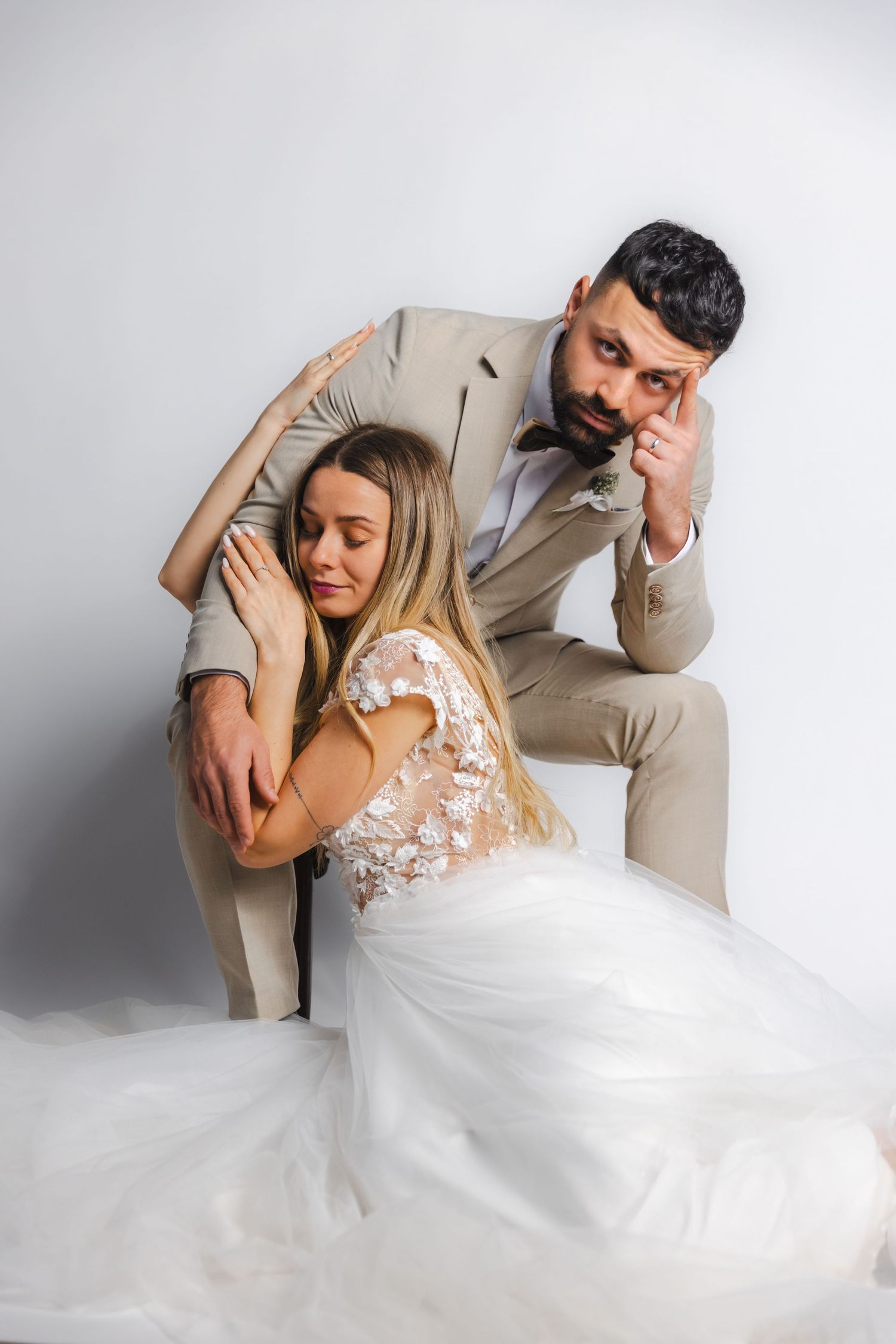 Wedding couple in white dress and beige suit dancing dramatically on white background.