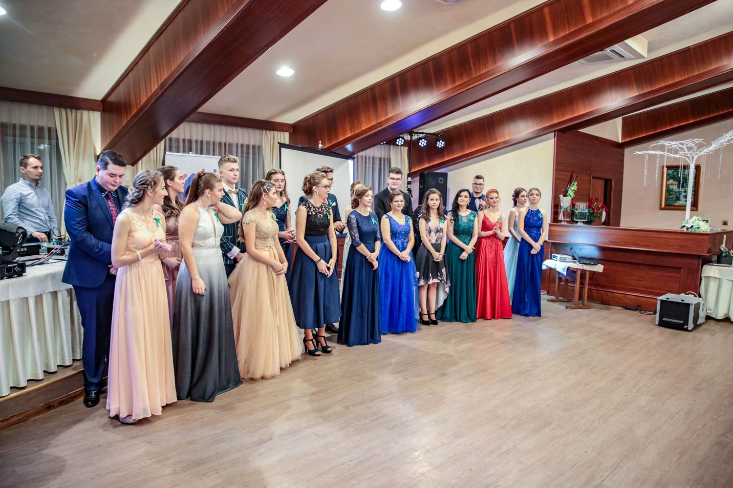 Panoramic view of formal event in wood-paneled ballroom with guests in evening attire.