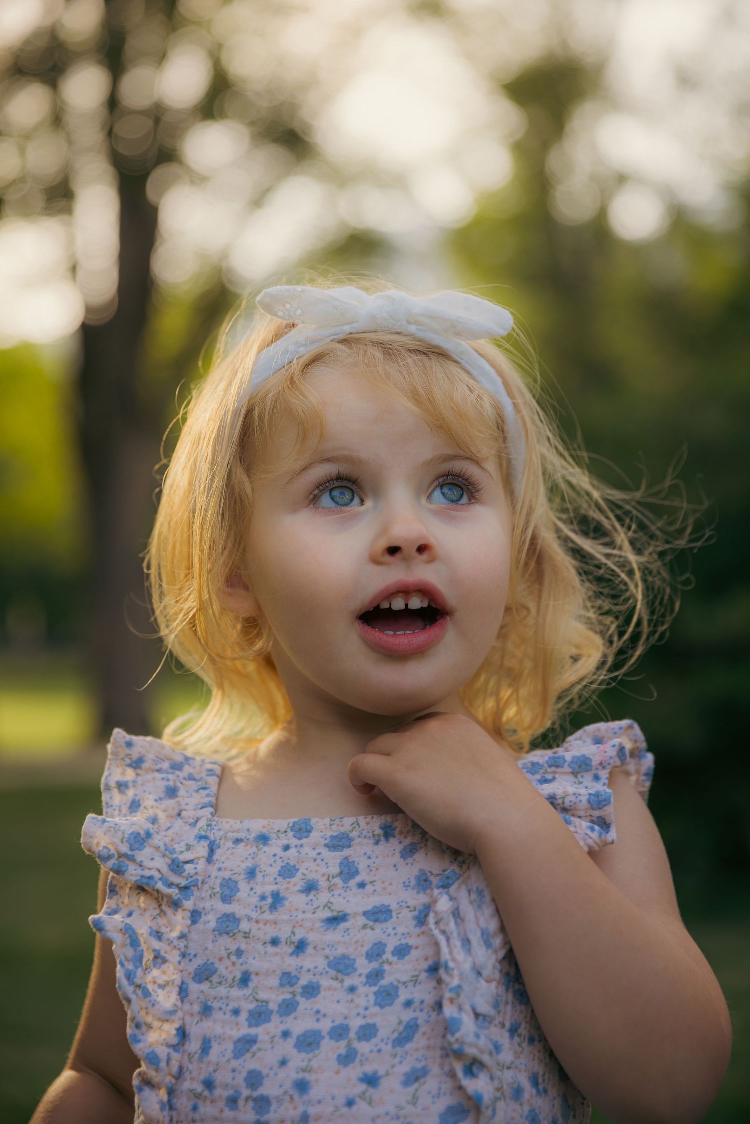 Child in floral dress making playful expressions outdoors during sunset.