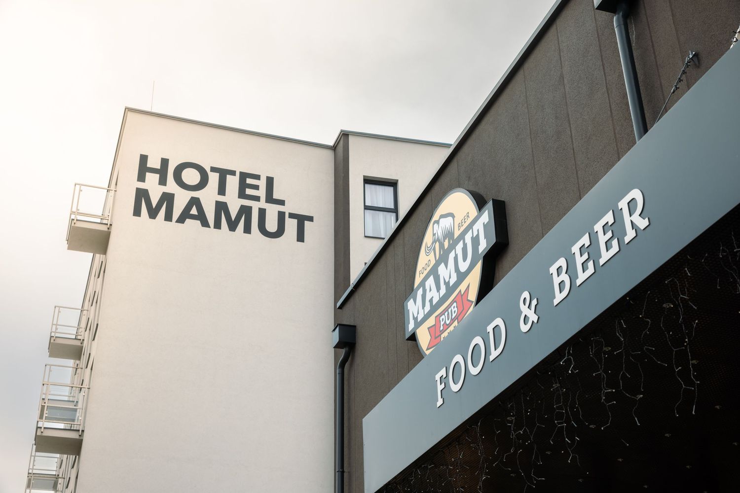Exterior signage of Hotel Mamut and restaurant with modern typography against grey building facade.