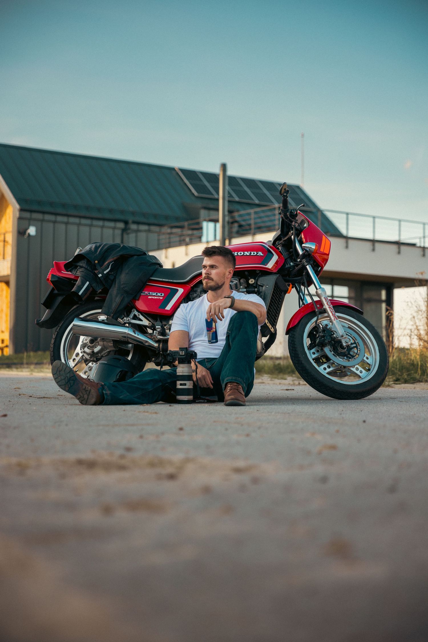 Casual portrait of person sitting beside red motorcycle during golden hour.