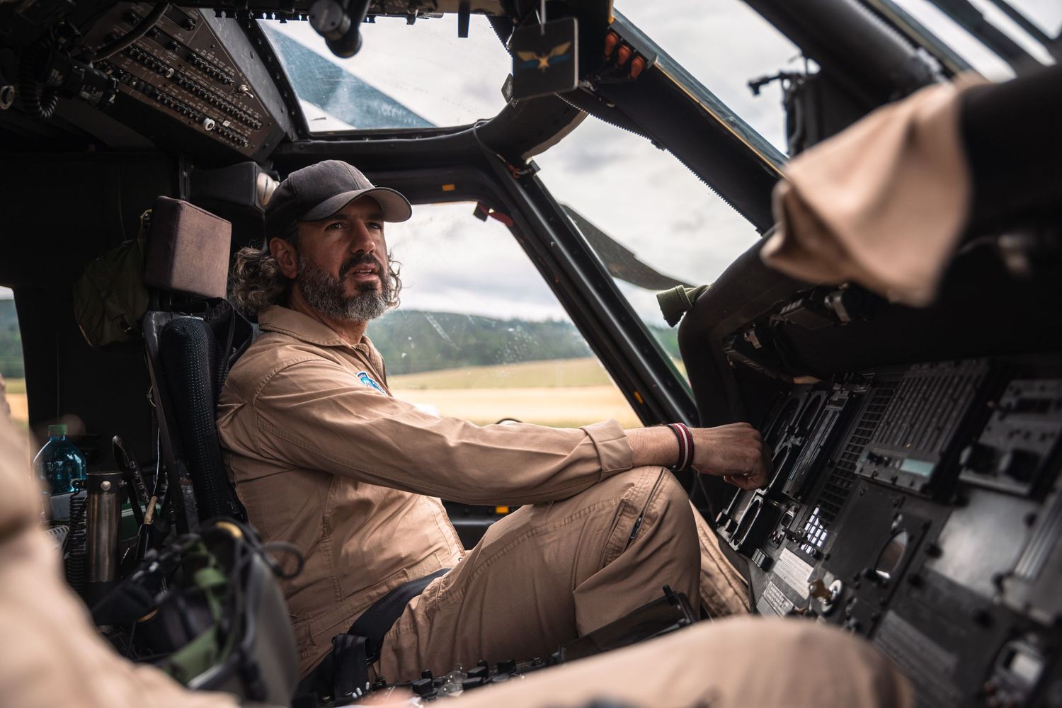 Pilots in tan flight suits operate controls inside military helicopter cockpit.