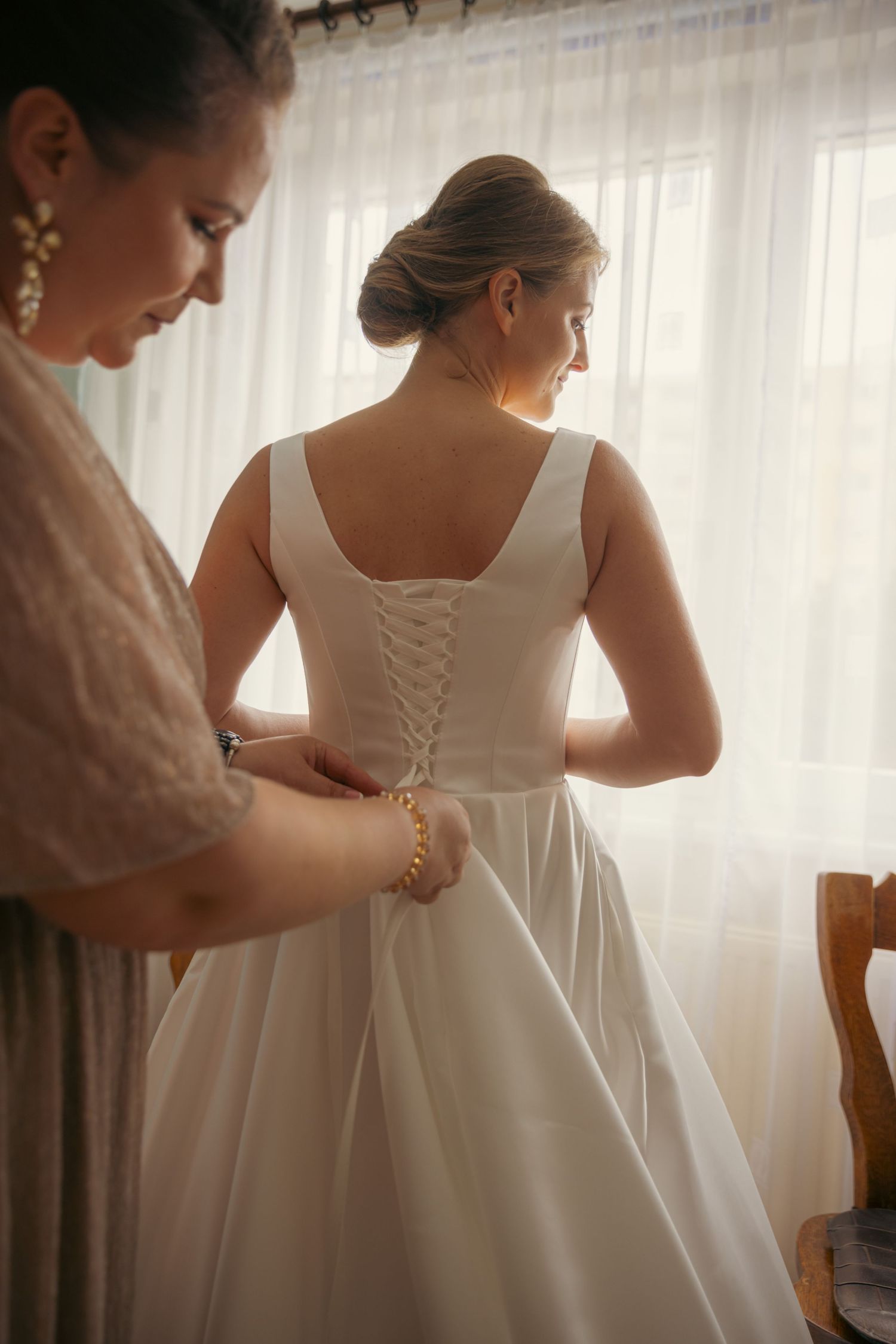 Close-up details of a white wedding dress being laced up from behind.