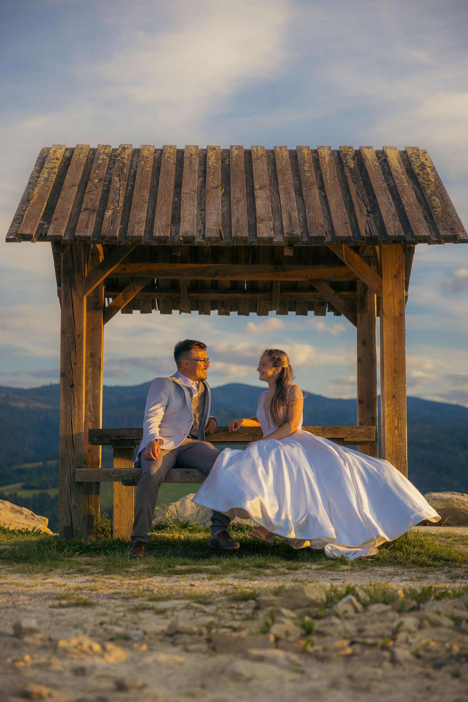 Couple resting under rustic wooden shelter with panoramic mountain views.