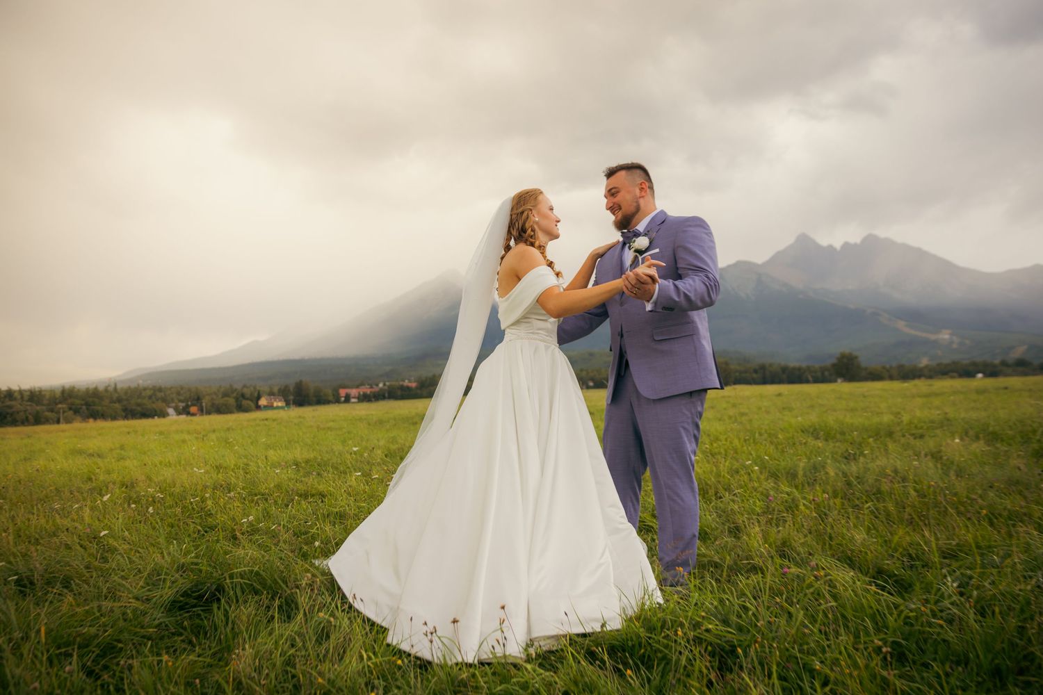 Wedding couple walking through green meadow with mountains in background.