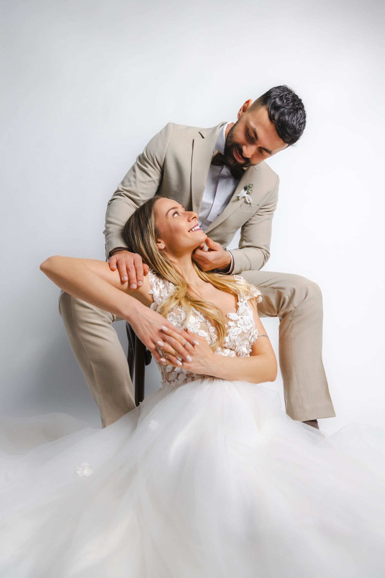 Romantic wedding couple poses in elegant dips against white studio backdrop.