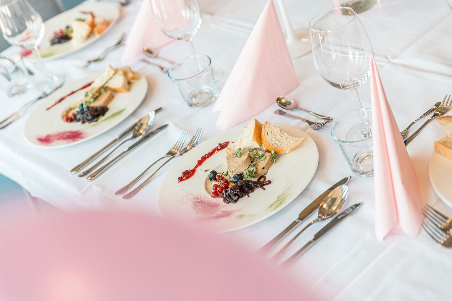 Elegant table setting with pink napkins and formal dinnerware on white tablecloth.