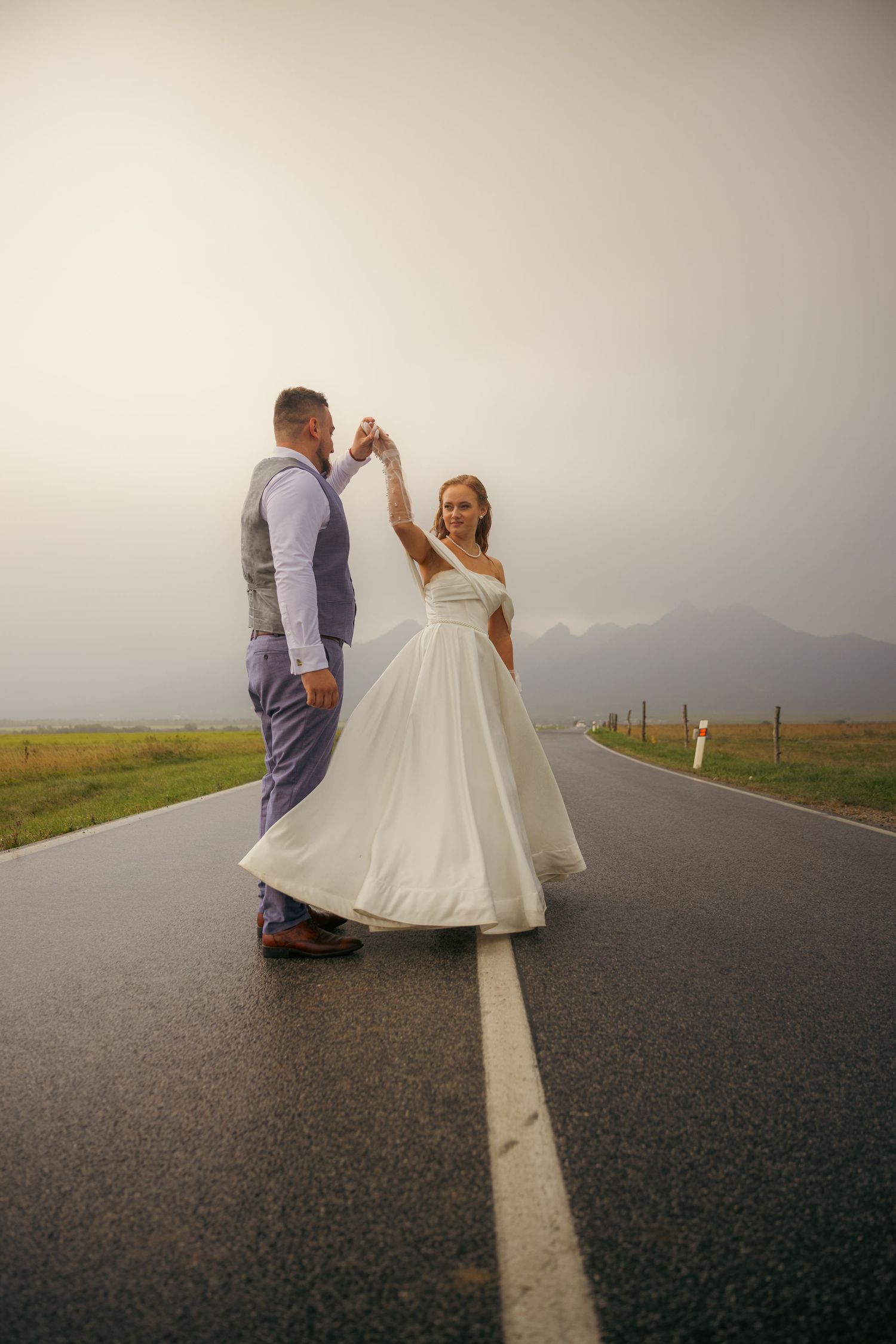 A couple poses on a scenic mountain road with the bride's dress flowing in the wind.