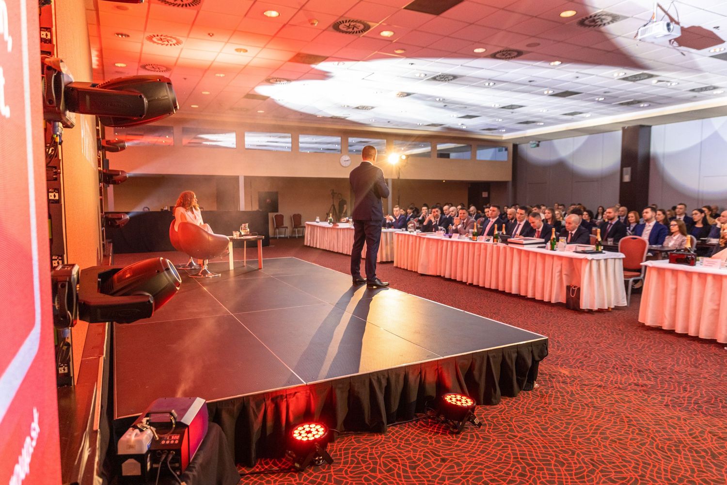 Conference venue with red-lit walls and multiple presentation screens.