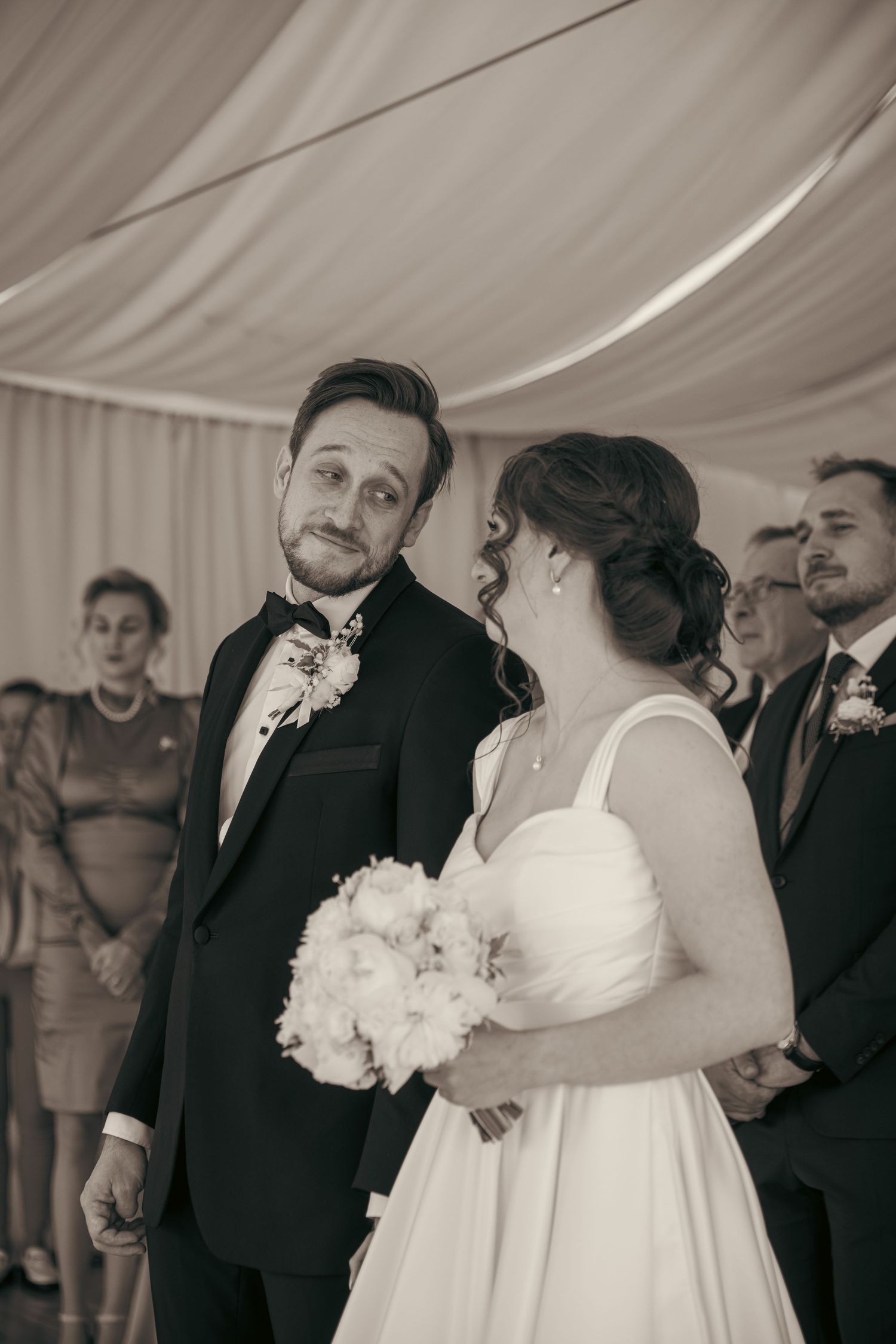 Wedding couple sharing their first dance under a white tent surrounded by guests.