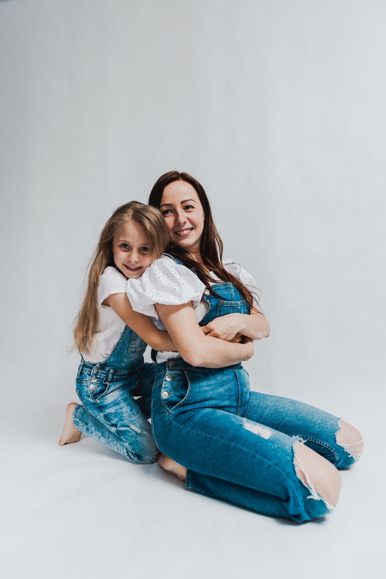 Casual lifestyle portrait of two people in denim and white on light background.