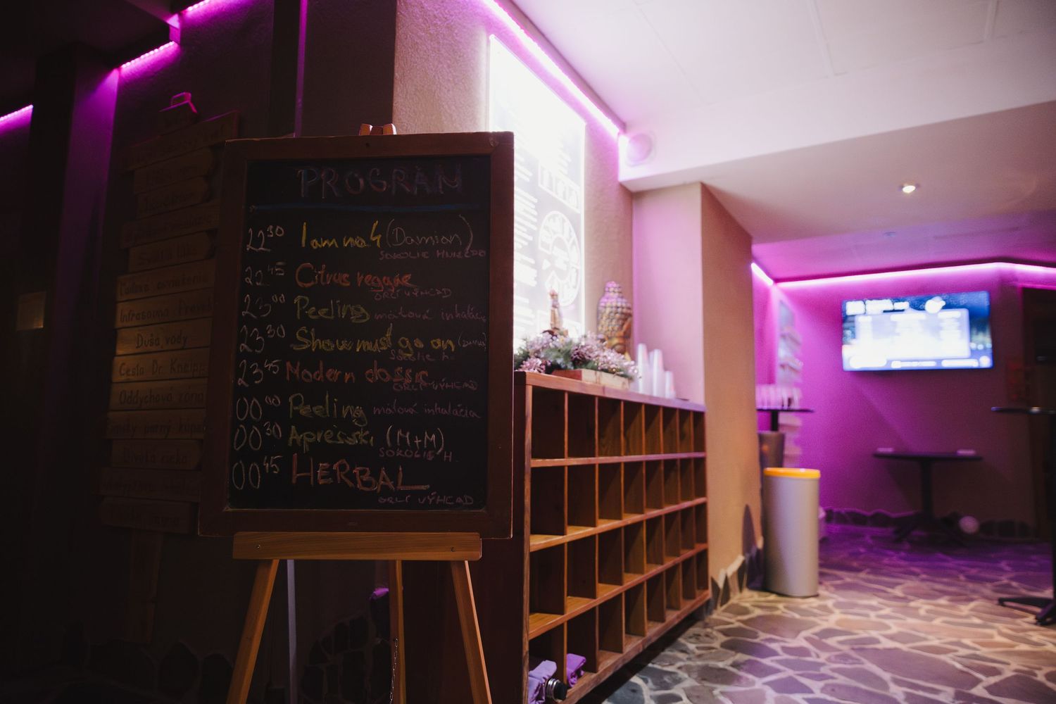 Purple-lit interior with chalkboard menu and wooden shelving units along the wall.