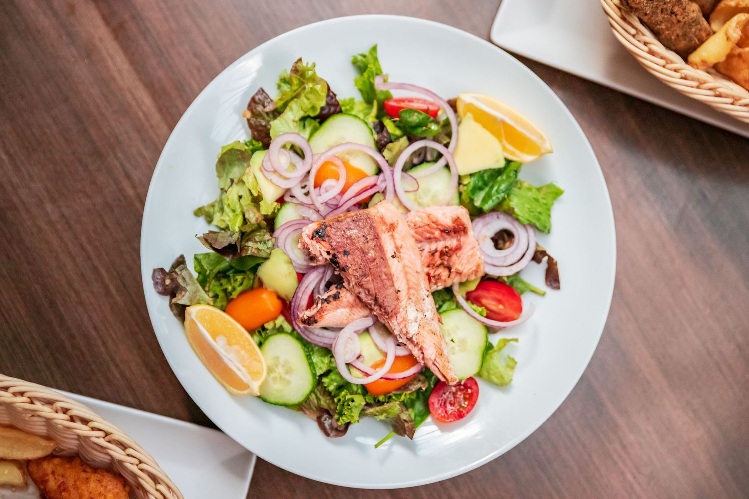 Fresh salad plates with mixed greens, vegetables and protein arranged on white dishes.