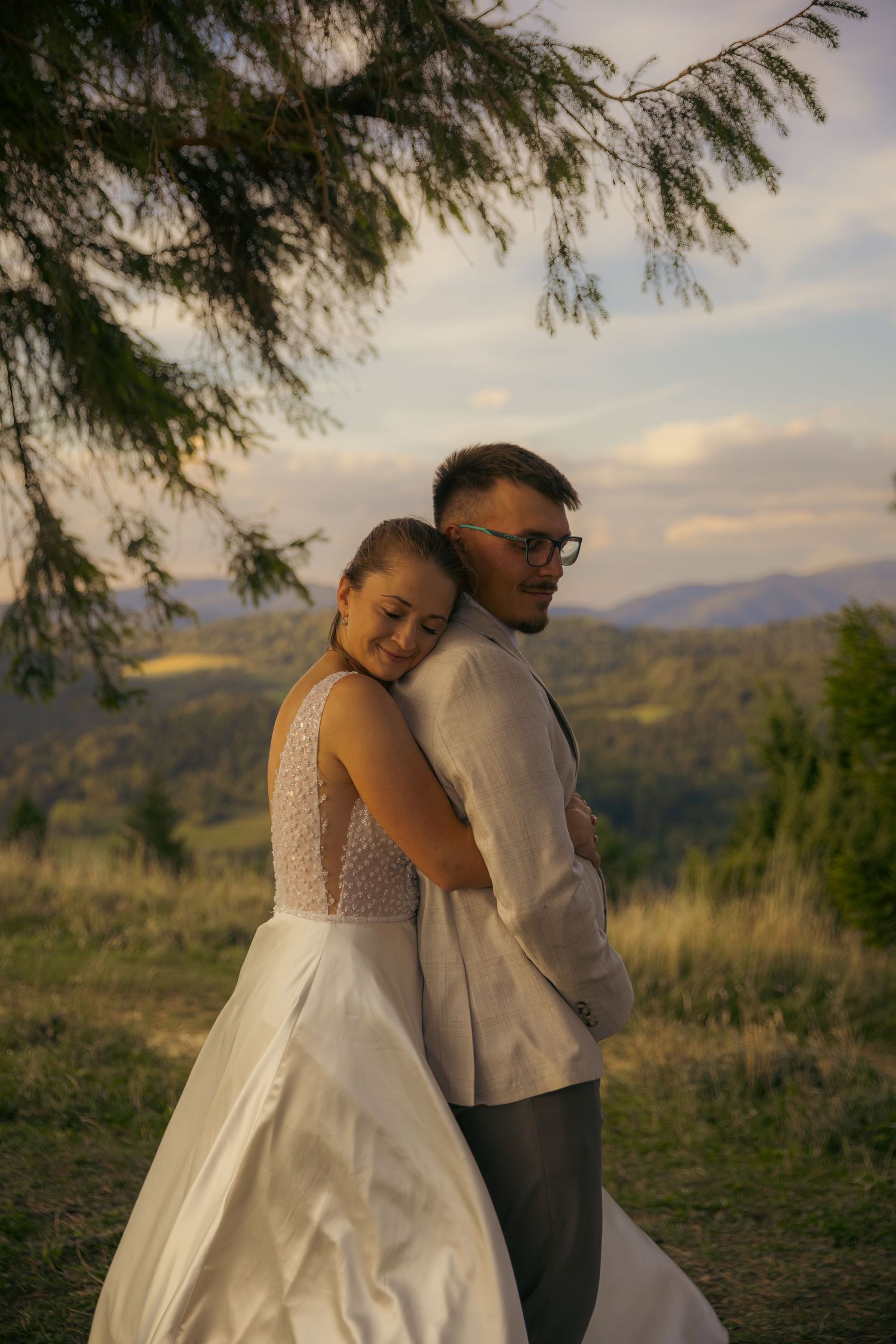 Intimate wedding moment captured under pine trees with mountain views at dusk.