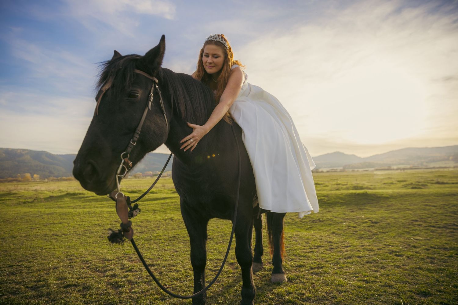 Majestic black horse with riders in open field against mountain backdrop.