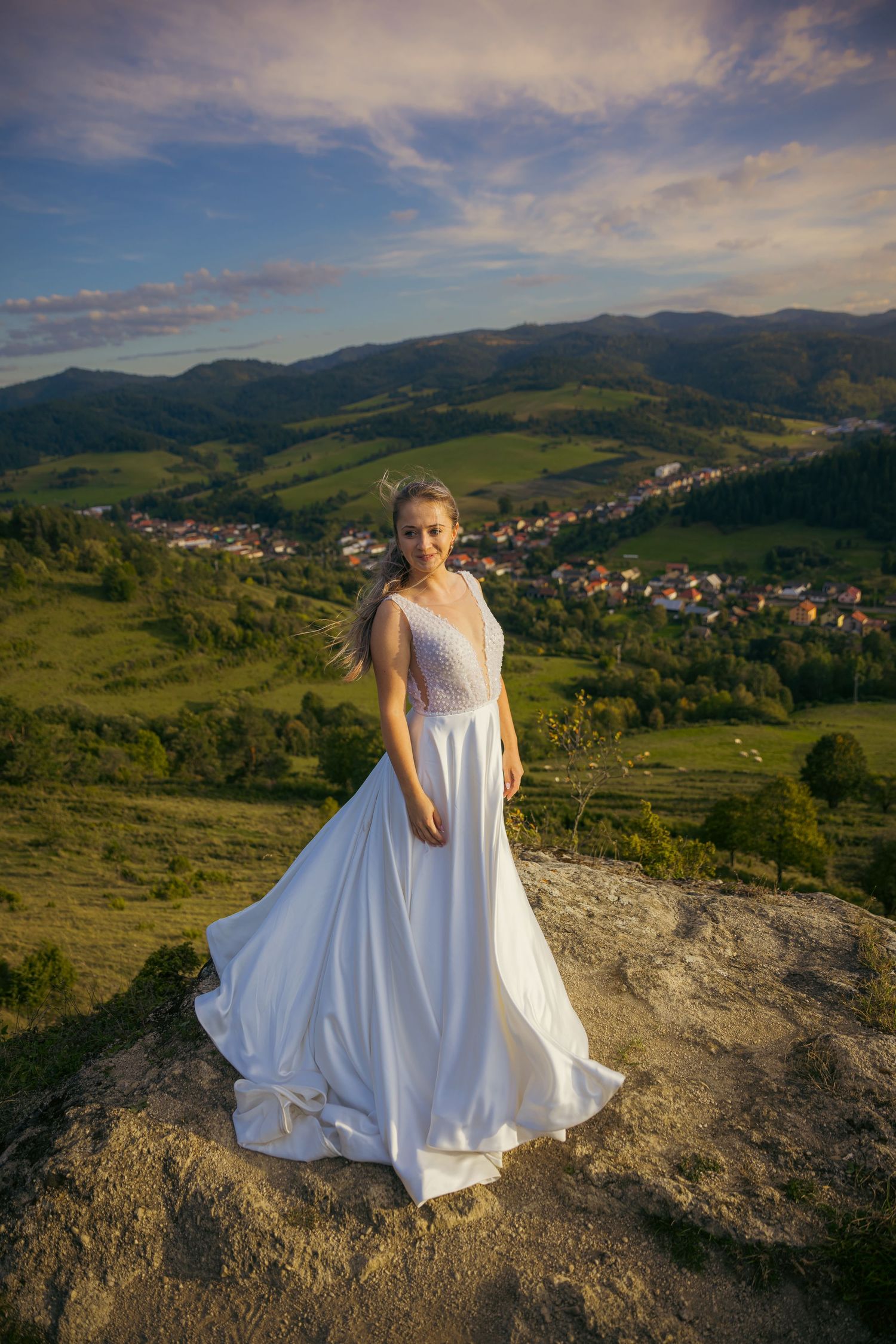 A bride twirls her white dress on a hilltop overlooking a mountain village.