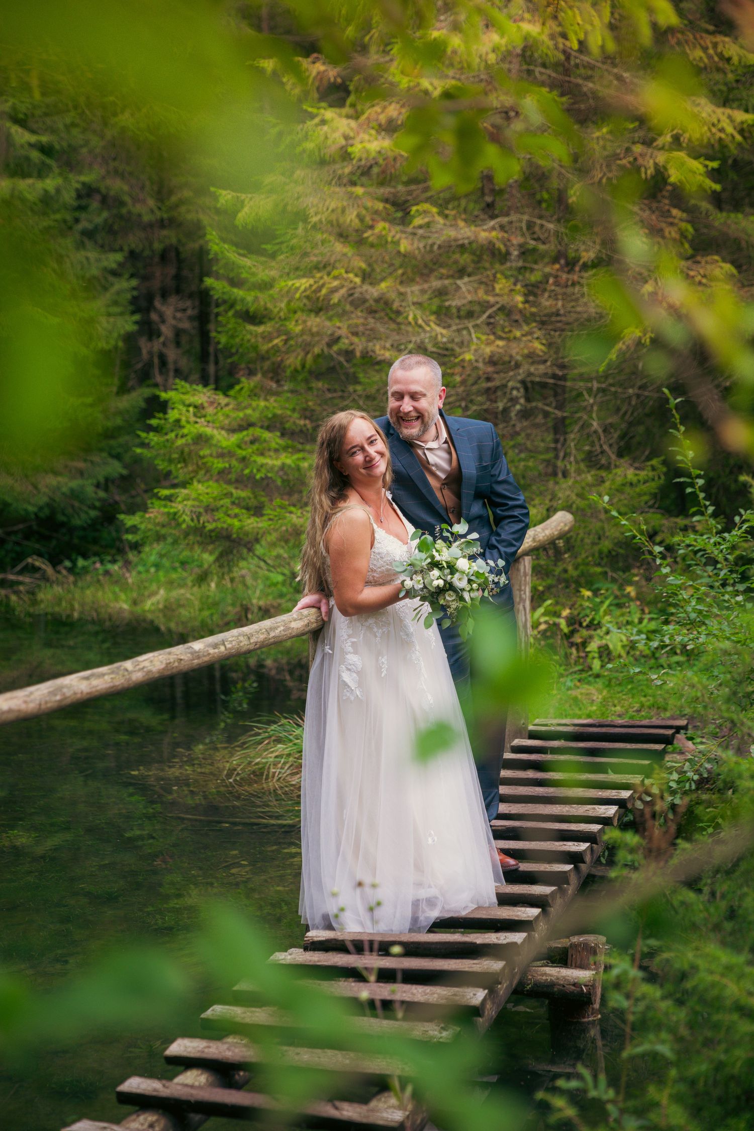 Wedding couple shares romantic moment on wooden bridge surrounded by lush forest.