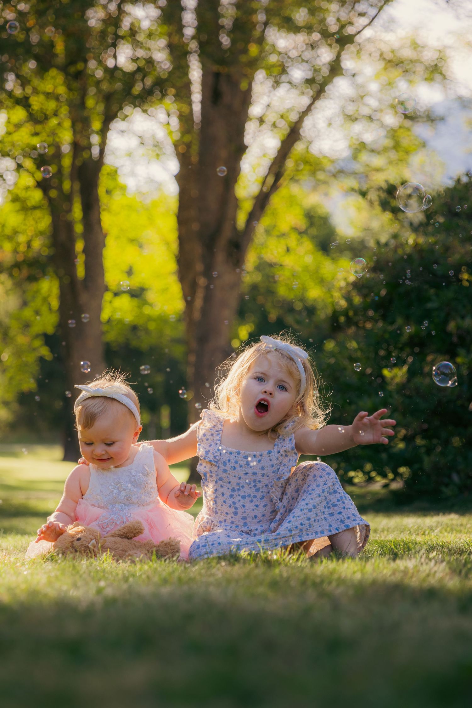Two children playing and rolling on grass during golden hour in a park.