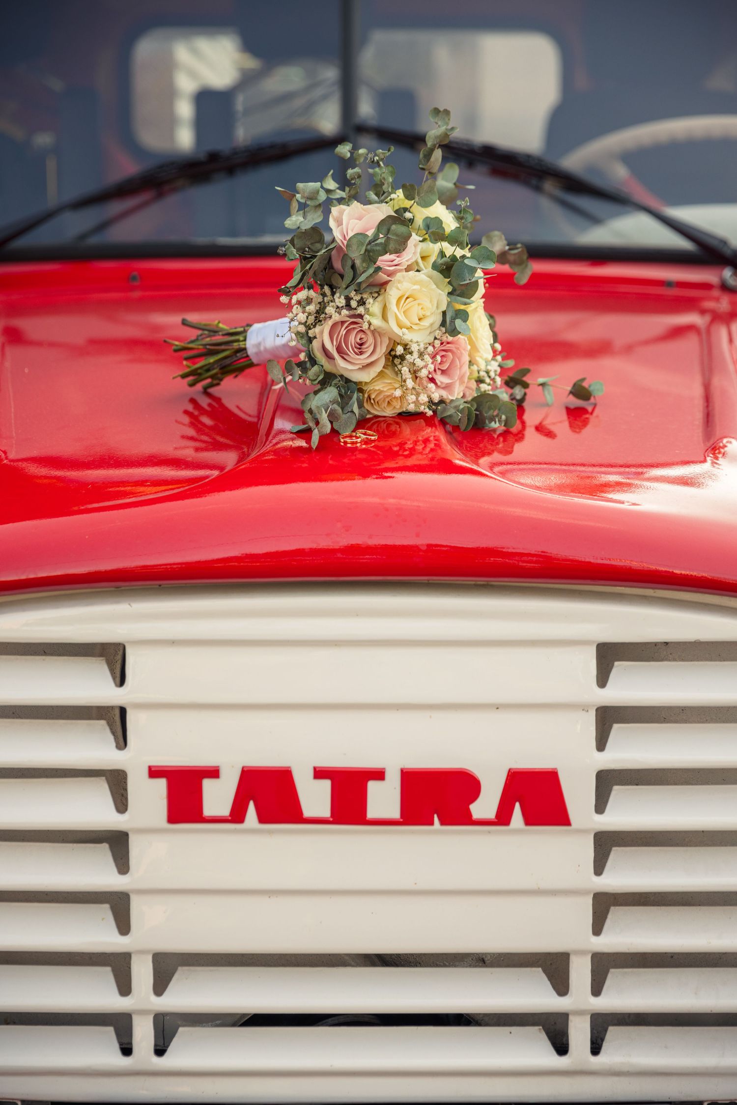 Wedding bouquet rests on vintage red Tatra truck grill.