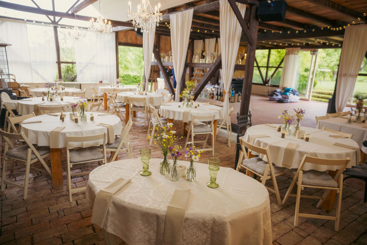Rustic wedding reception venue with round tables and wooden chairs set for dinner.