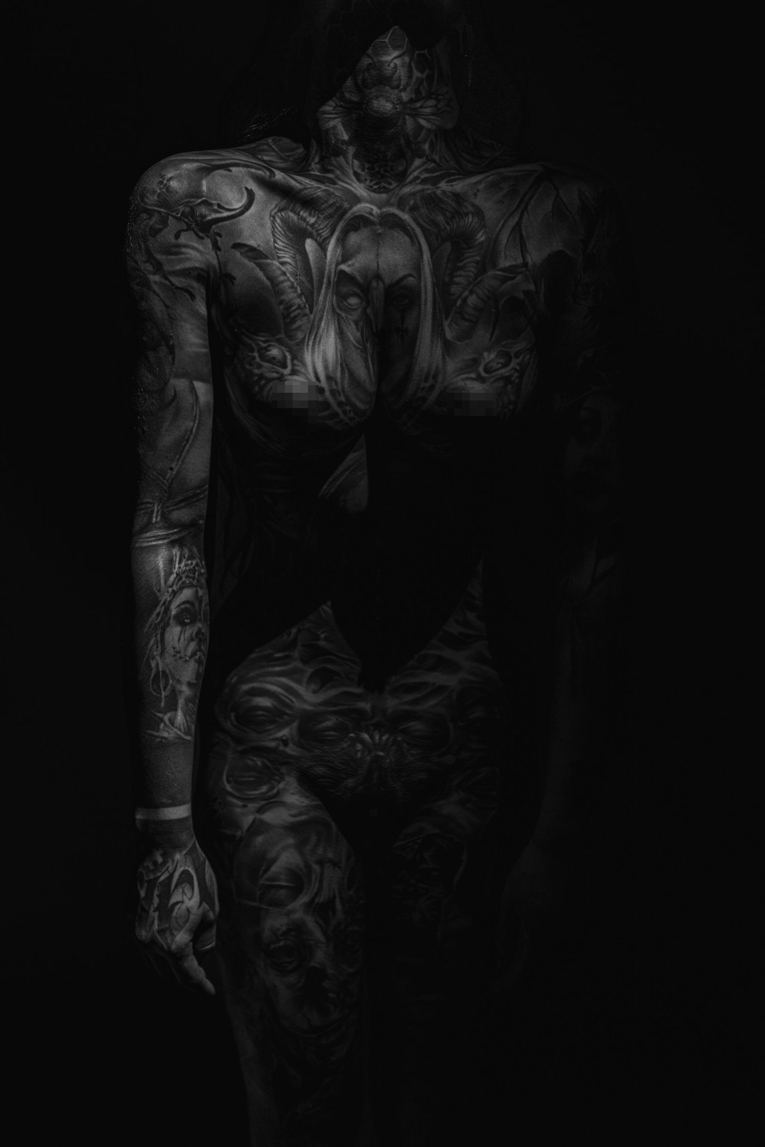 Artistic black and white portrait showing tattooed figure in dark shadows.