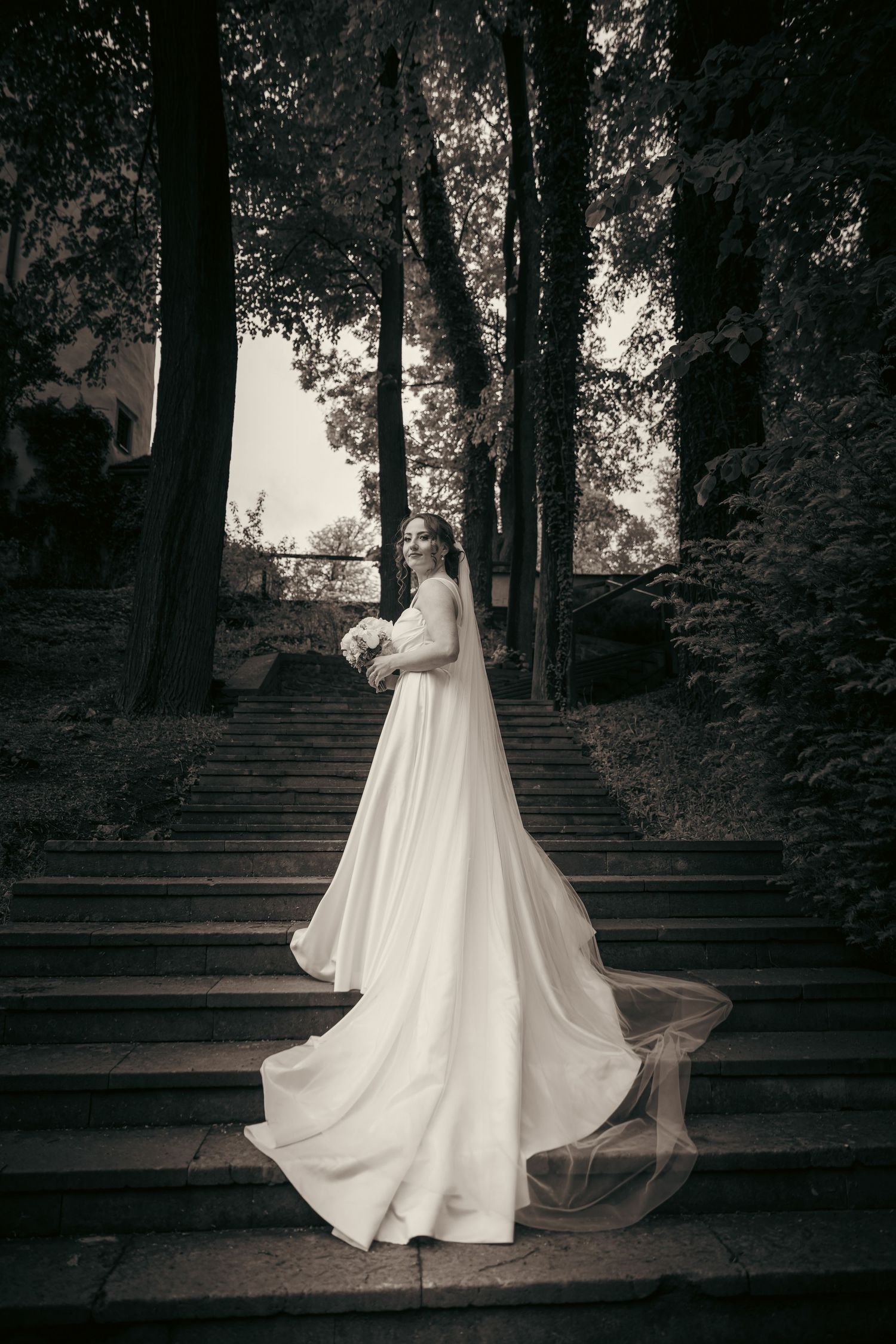 Elegant wedding dress photographed on stone steps in a moody black and white setting.
