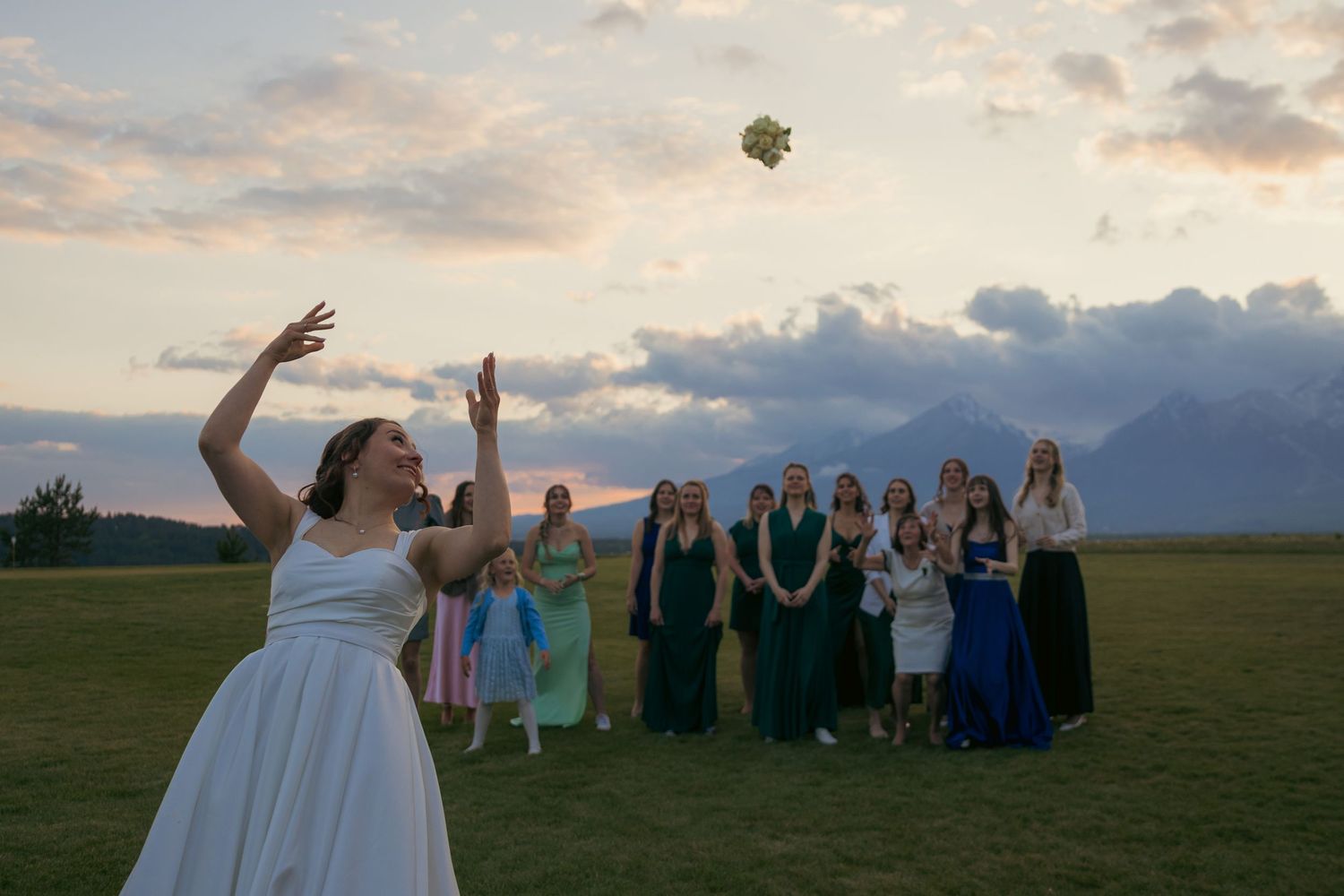 Wedding party poses in an outdoor field at sunset with mountains in the background.